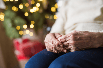 hands resting on a lap in front of a Christmas tree