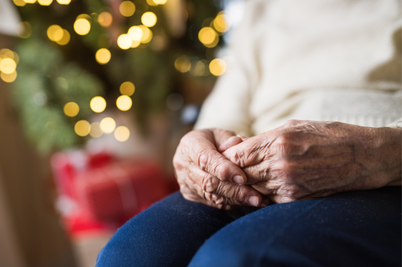 hands resting on a lap in front of a Christmas tree